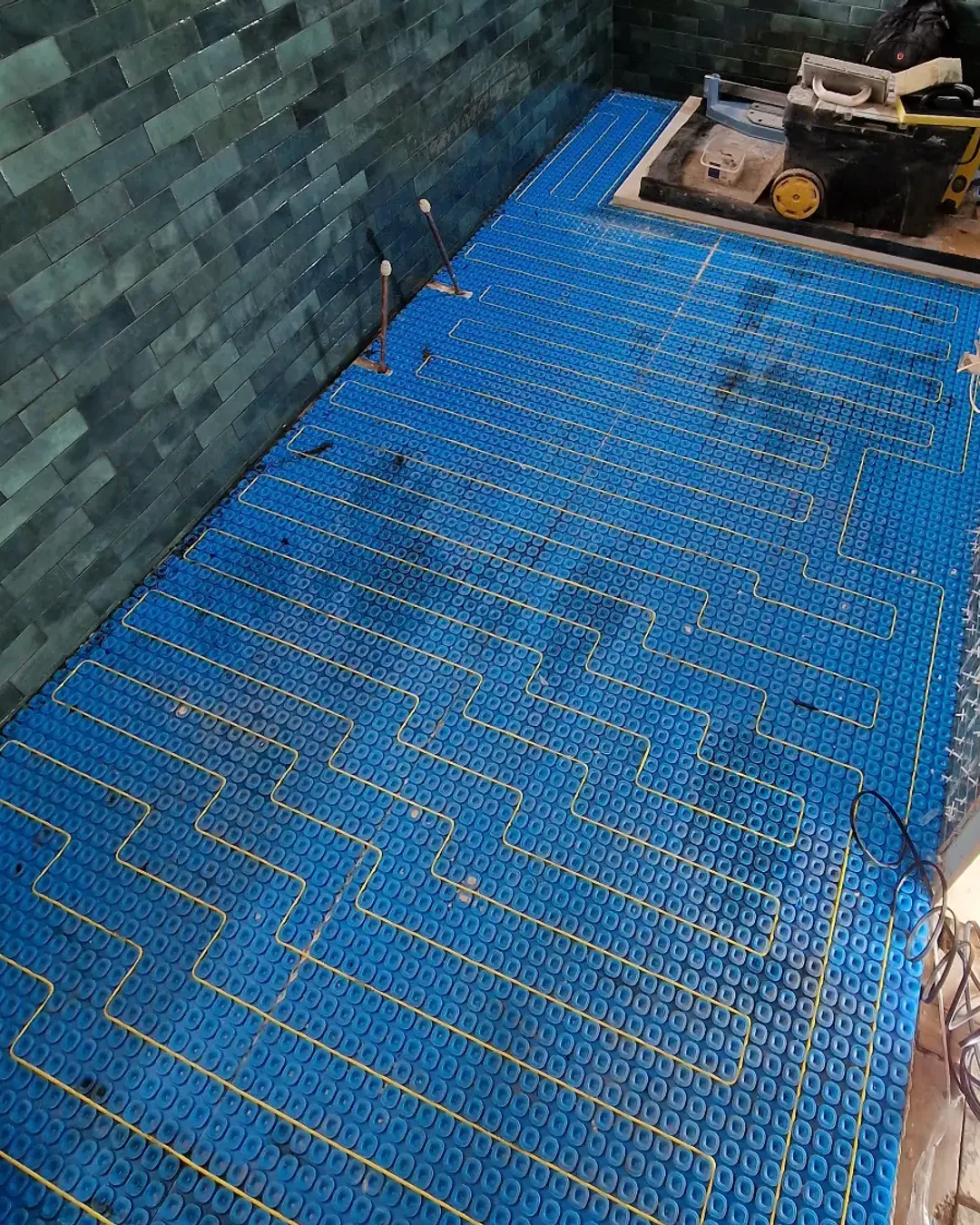 Electric underfloor heating cables arranged across a blue floor membrane during installation.