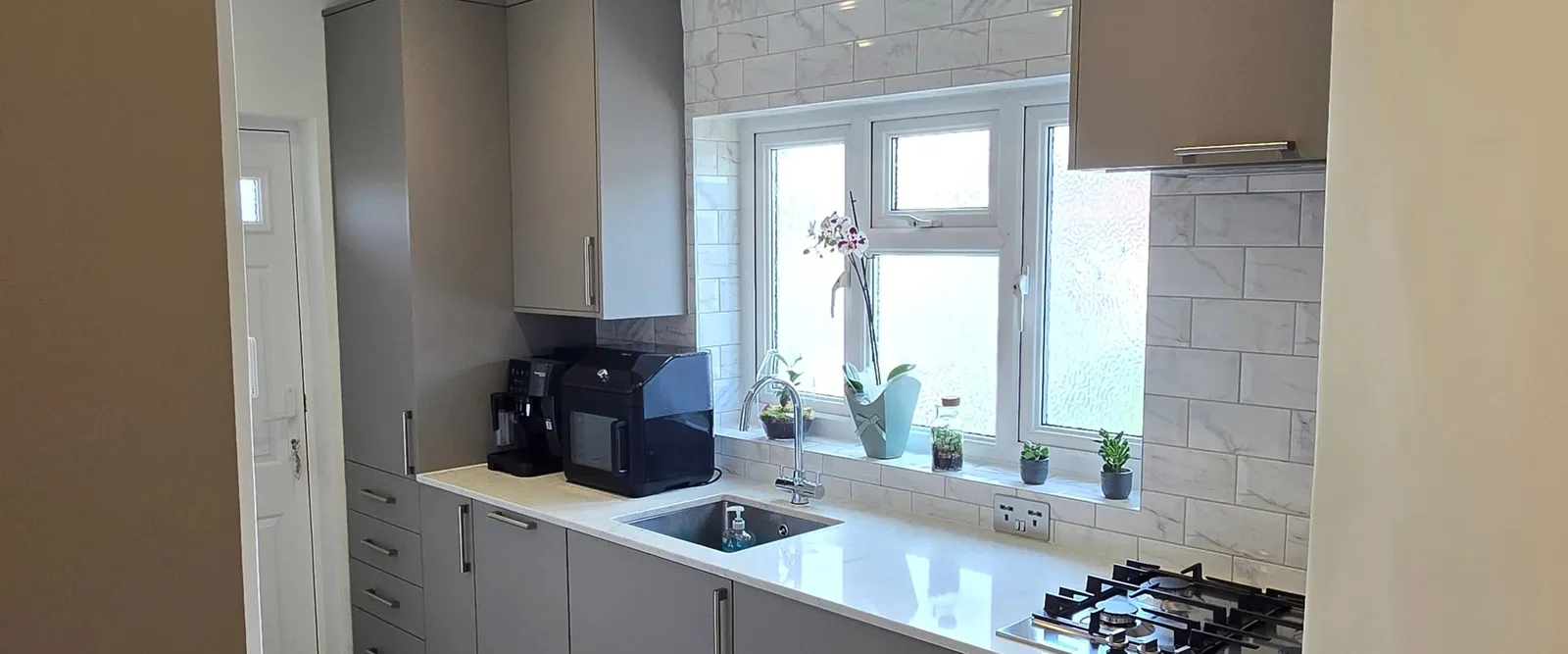Finished kitchen with a brickbond marble-effect splashback, grey cabinetry and large-format floor tiles.