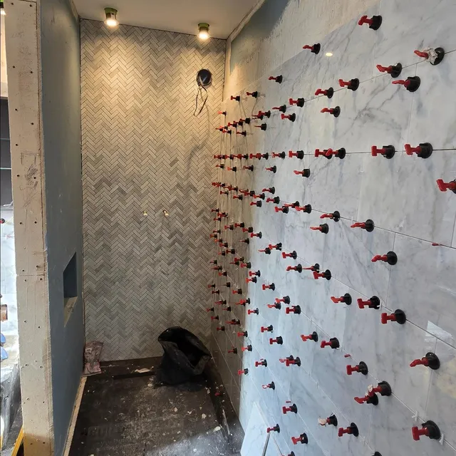 Shower corner with herringbone wall tiles beside large marble-effect tiles held by levelling clips.