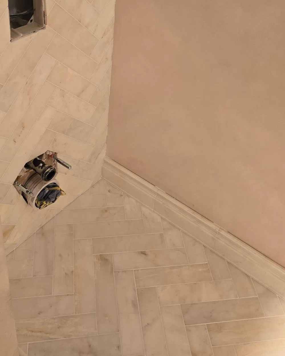 Corner view of herringbone marble-effect floor and wall tiles.