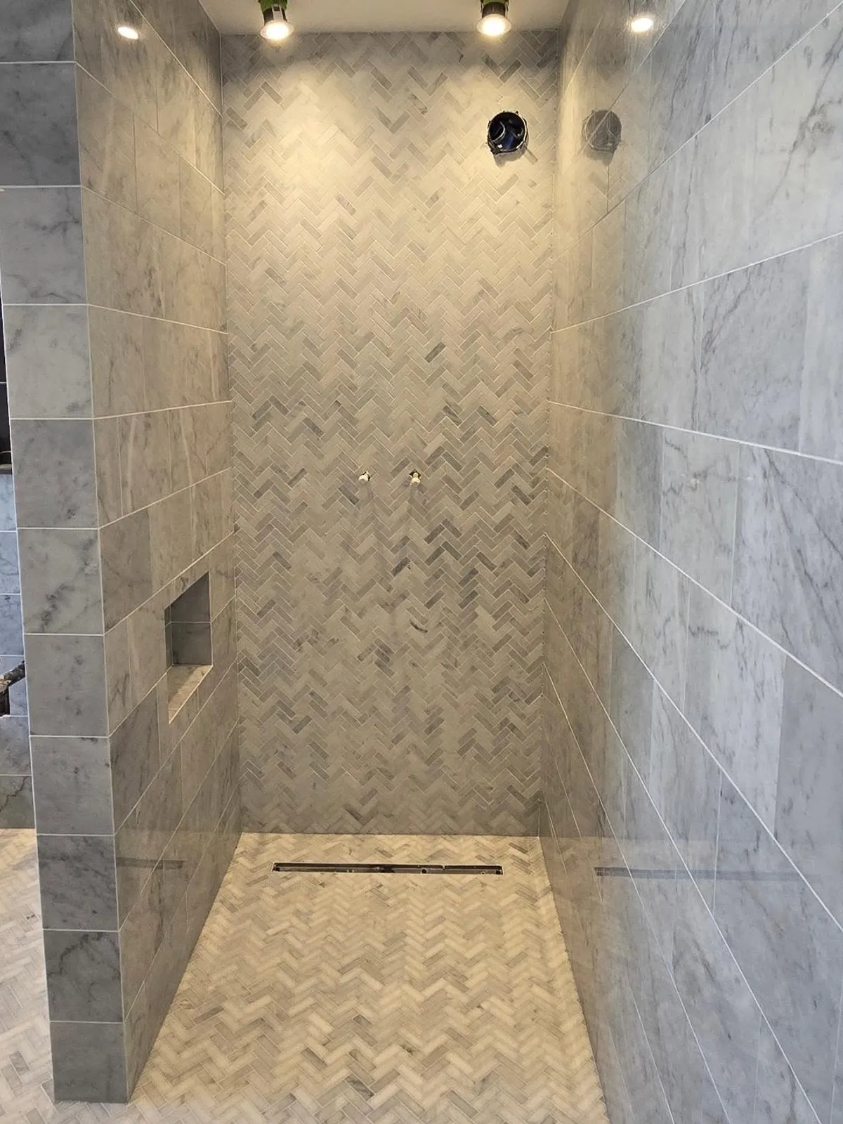 Walk-in shower with marble-effect herringbone feature wall, matching floor and a recessed niche.