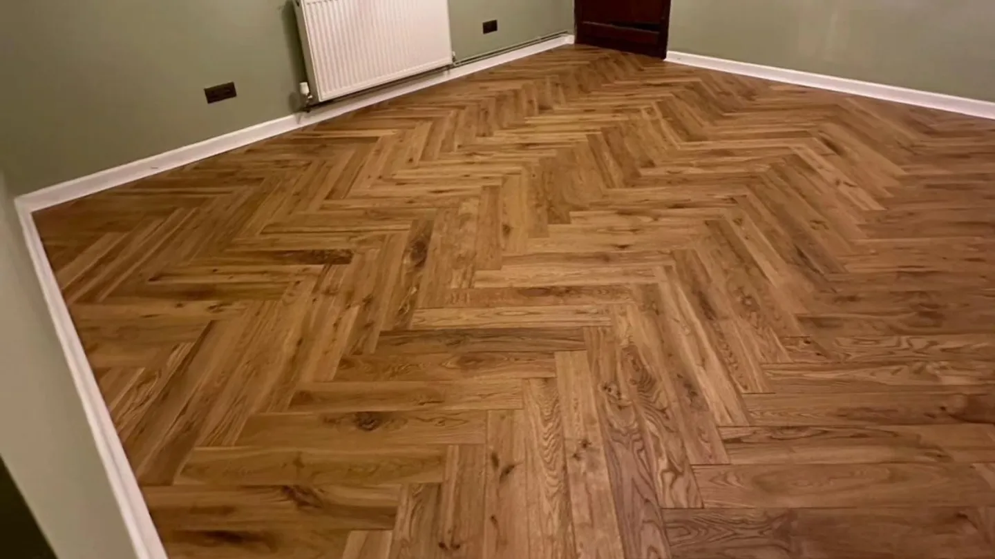 Wood-effect flooring laid in a herringbone pattern against sage green walls.