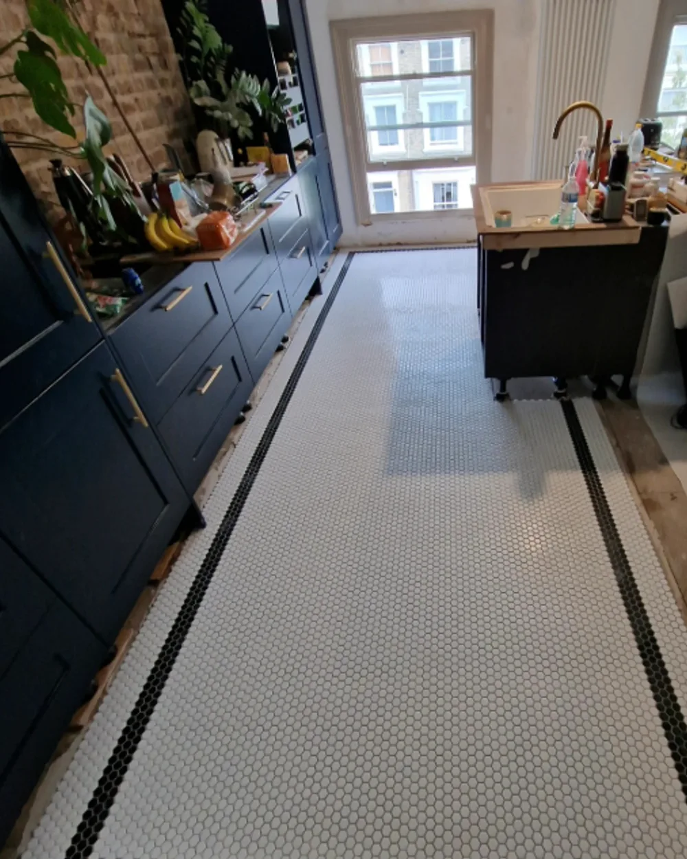 Kitchen floor with white hexagonal mosaic tiles and a black mosaic border beside navy cabinetry.