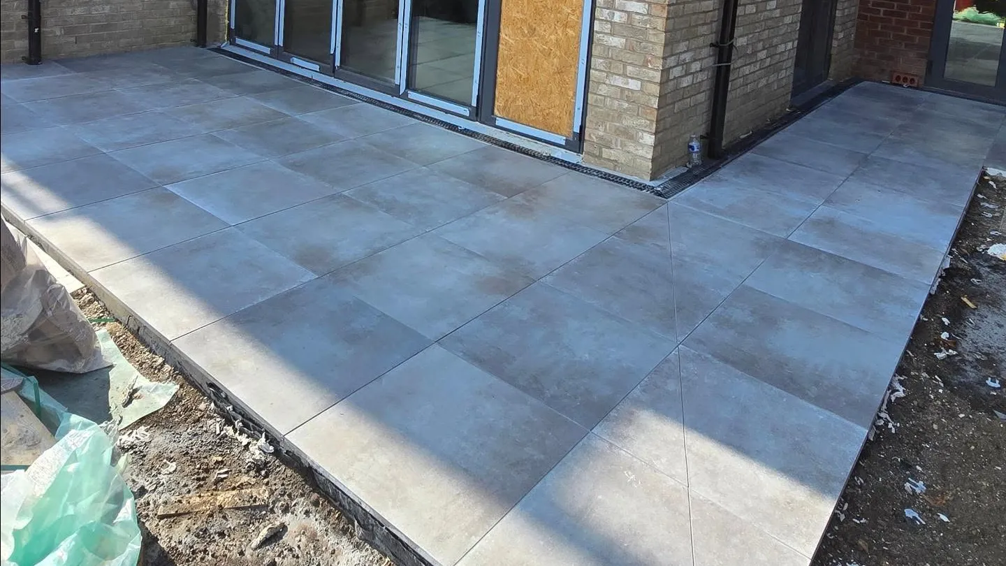 Exterior patio and side path with large-format stone-effect tiles beside a house elevation.