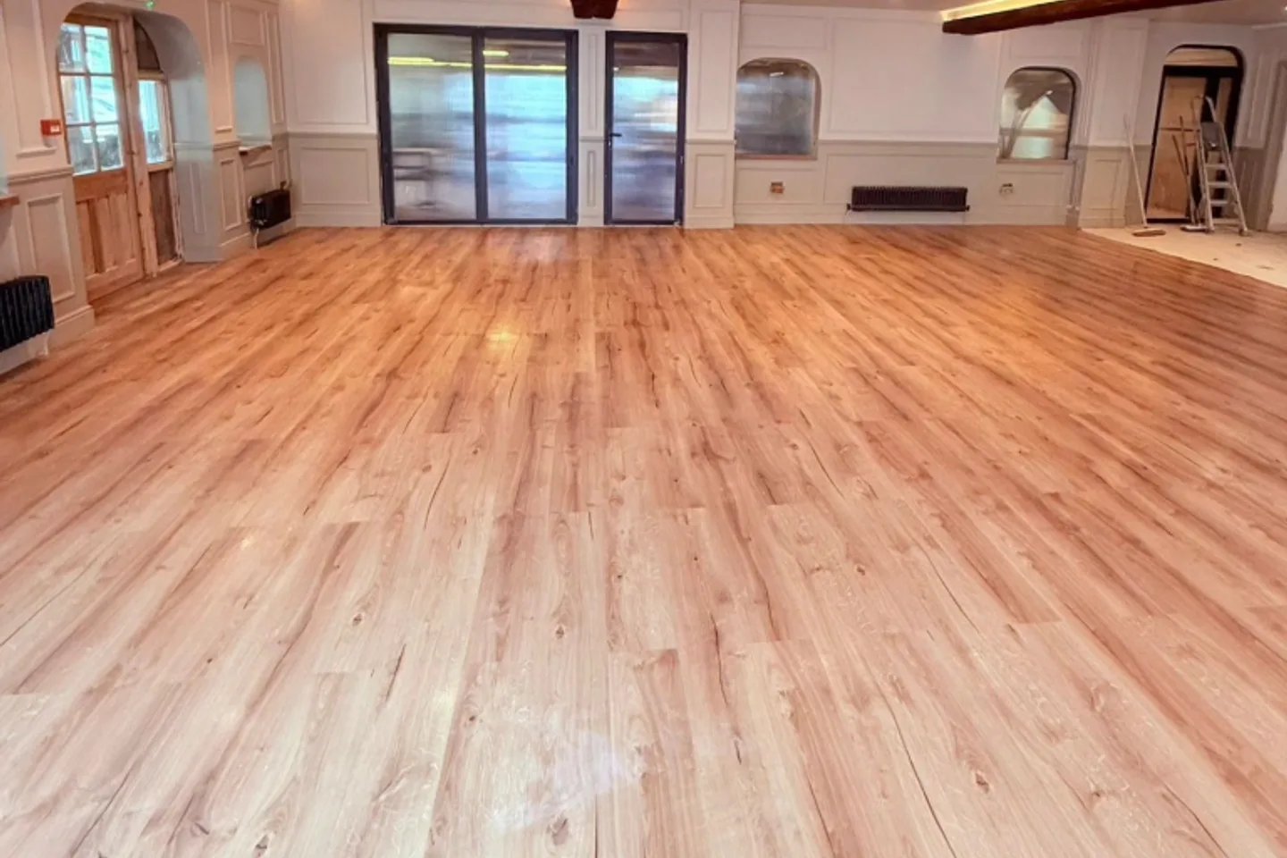 Large renovated interior with newly laid light wood-effect flooring and architectural detailing.