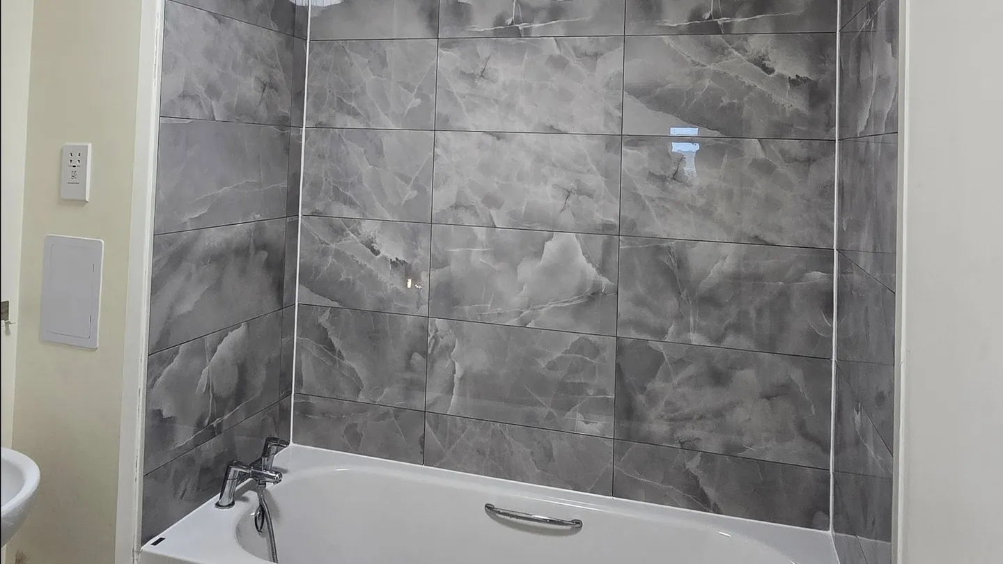 Completed bath surround with large grey marble-effect wall tiles.