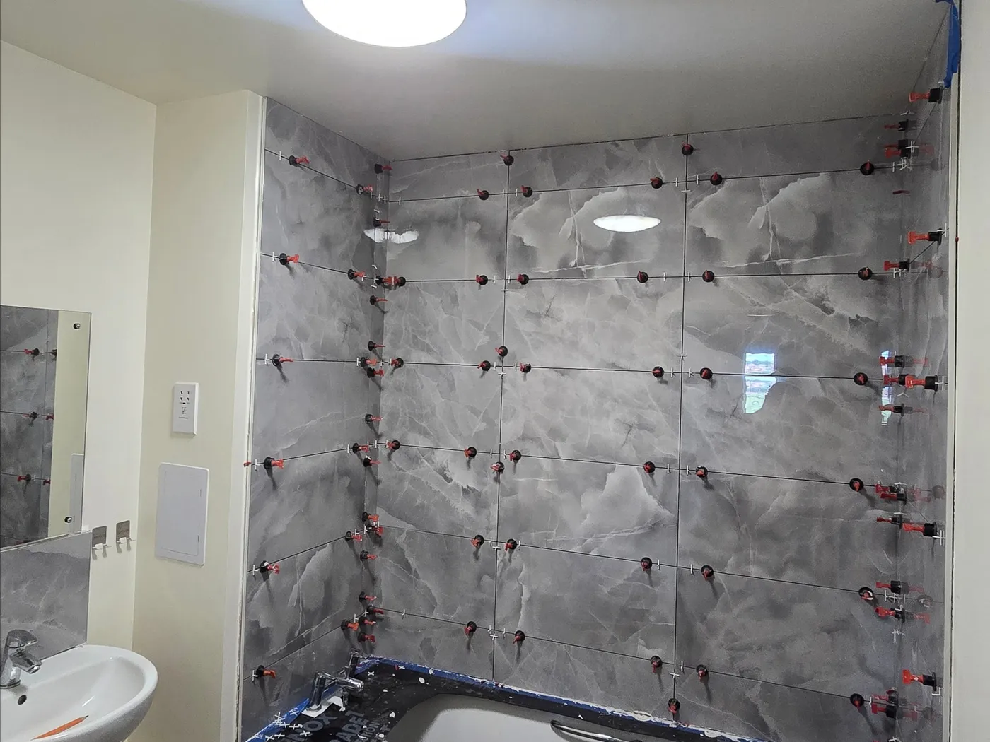 Bath surround with large grey marble-effect wall tiles during levelling installation.