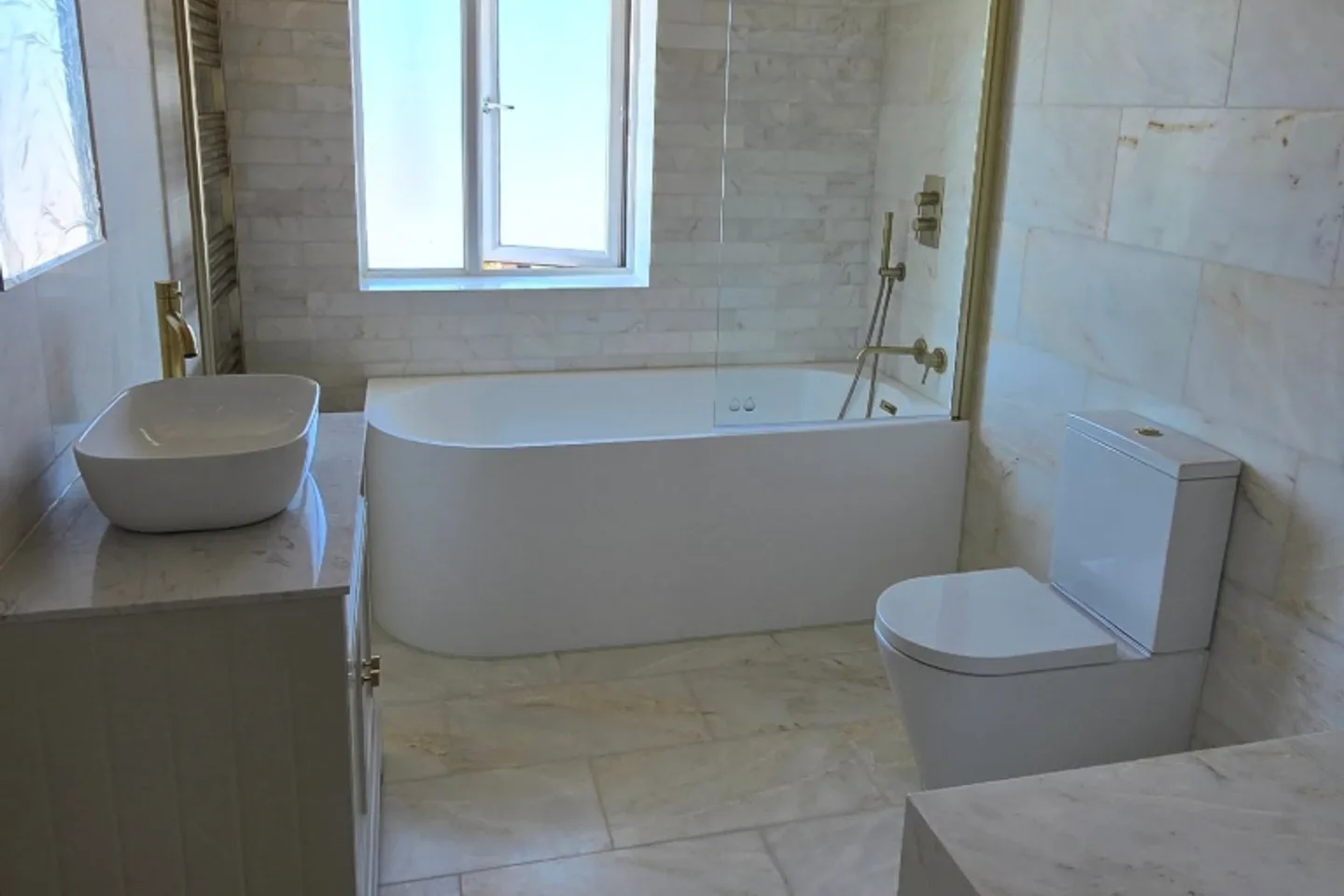 Bright finished bathroom with large-format marble-effect wall and floor tiles and gold fixtures.