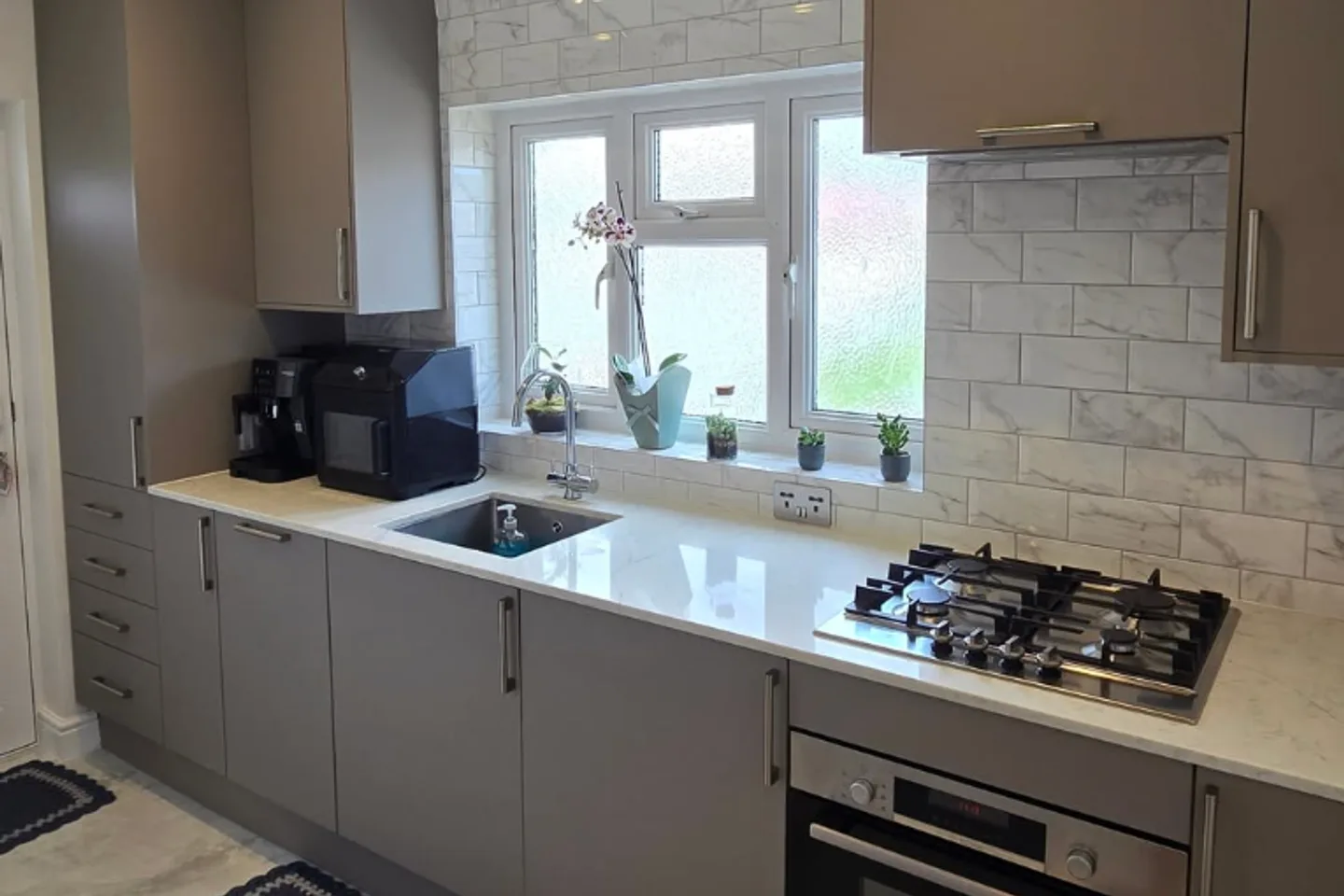 Finished kitchen with a marble-effect tiled splashback, stone-effect floor and coordinated cabinetry.