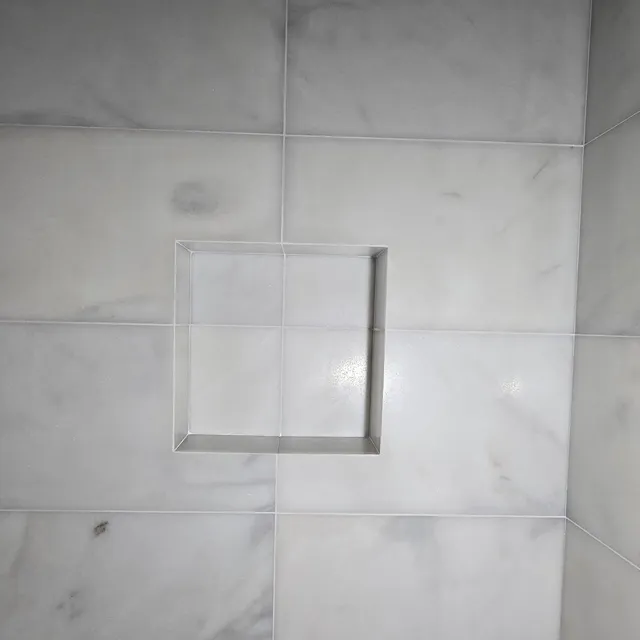 Close view of a recessed shower niche lined with marble-effect tiles.