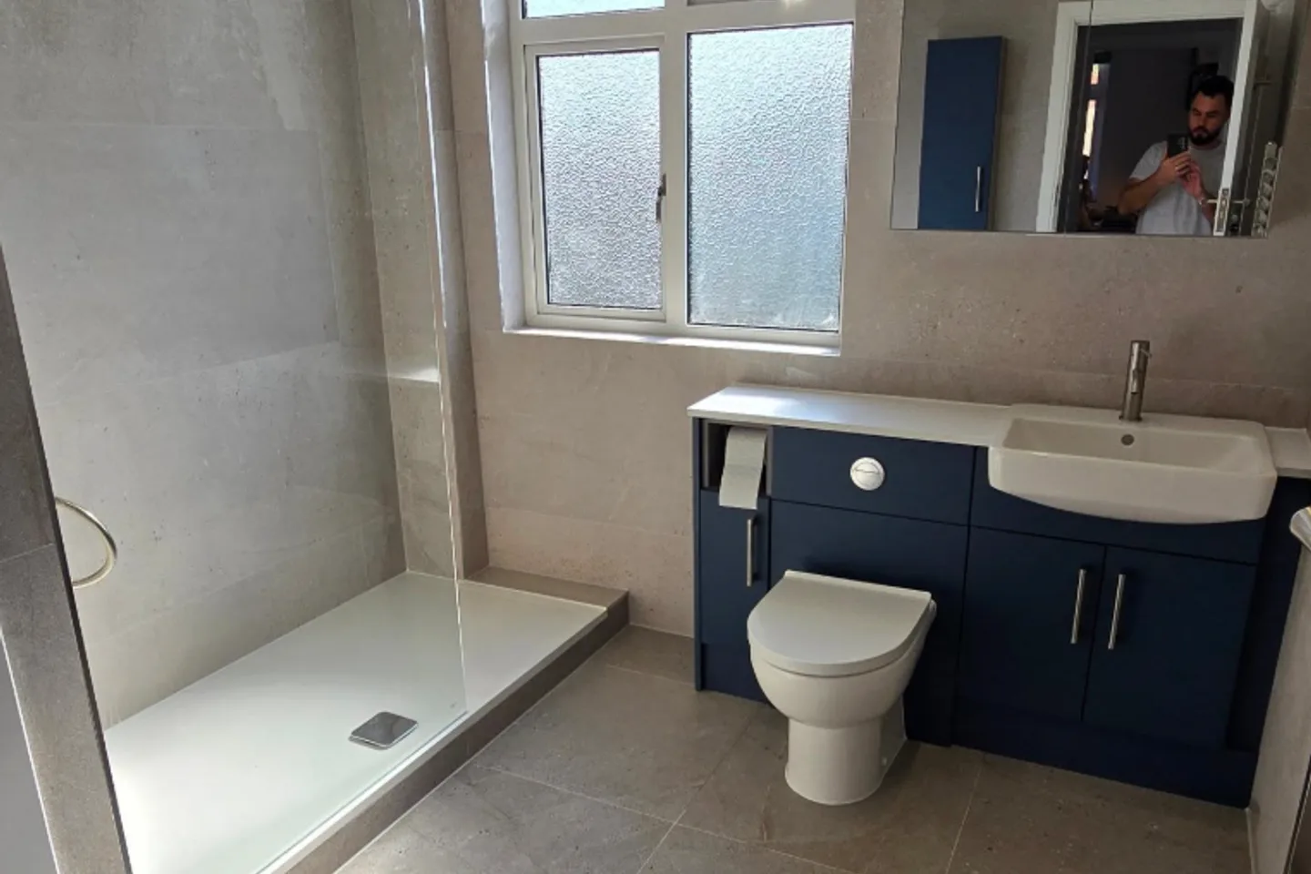Finished bathroom with large-format stone-effect tiles, walk-in shower and navy vanity unit.