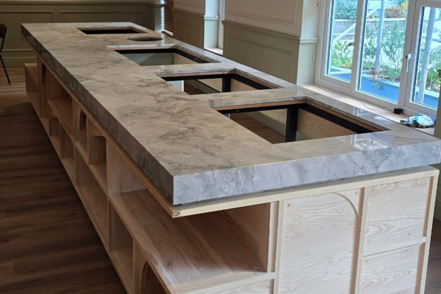 Stone worktop being set onto a custom timber kitchen island during a premium renovation.