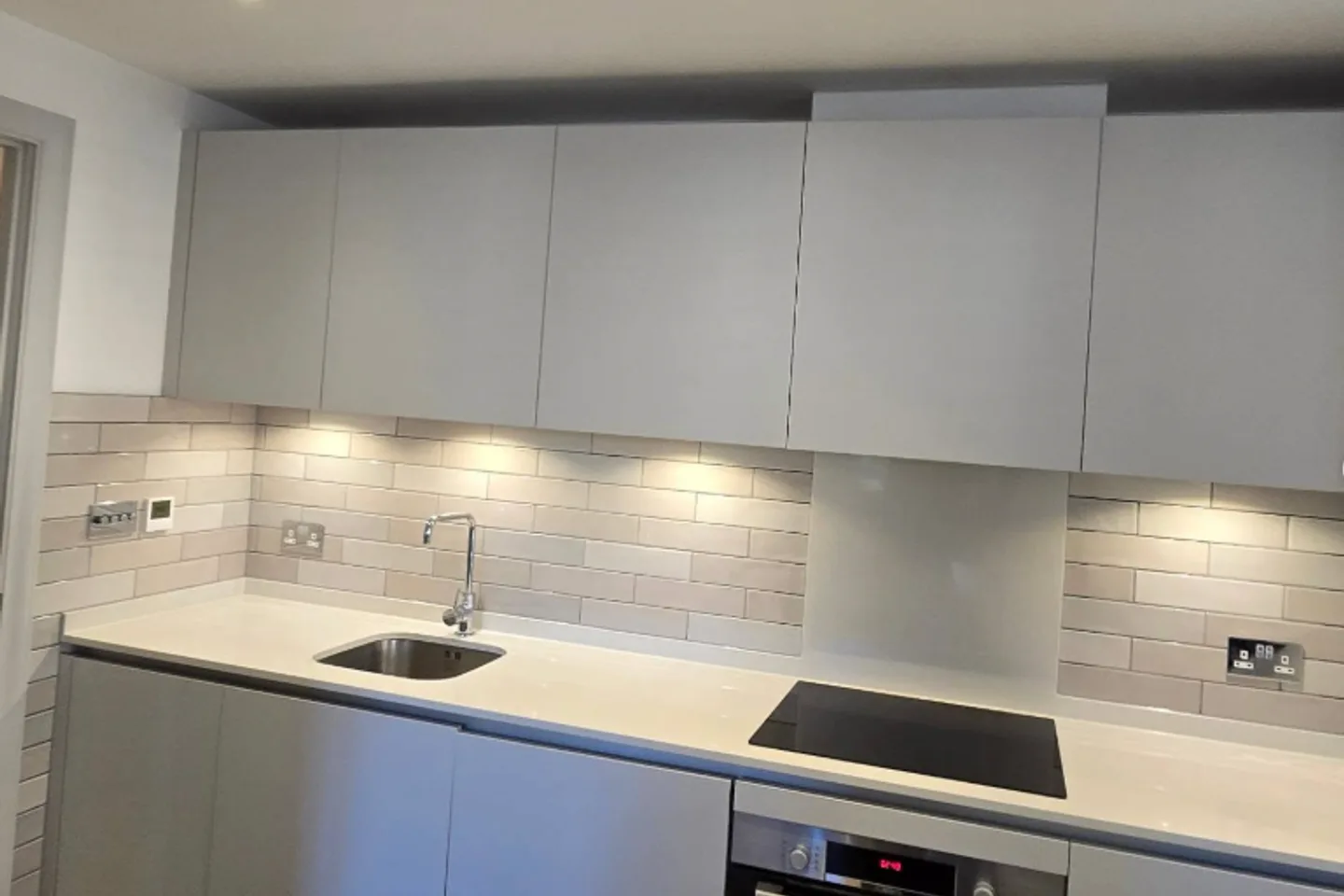 Contemporary kitchen with a grey subway-tiled splashback under warm under-cabinet lighting.