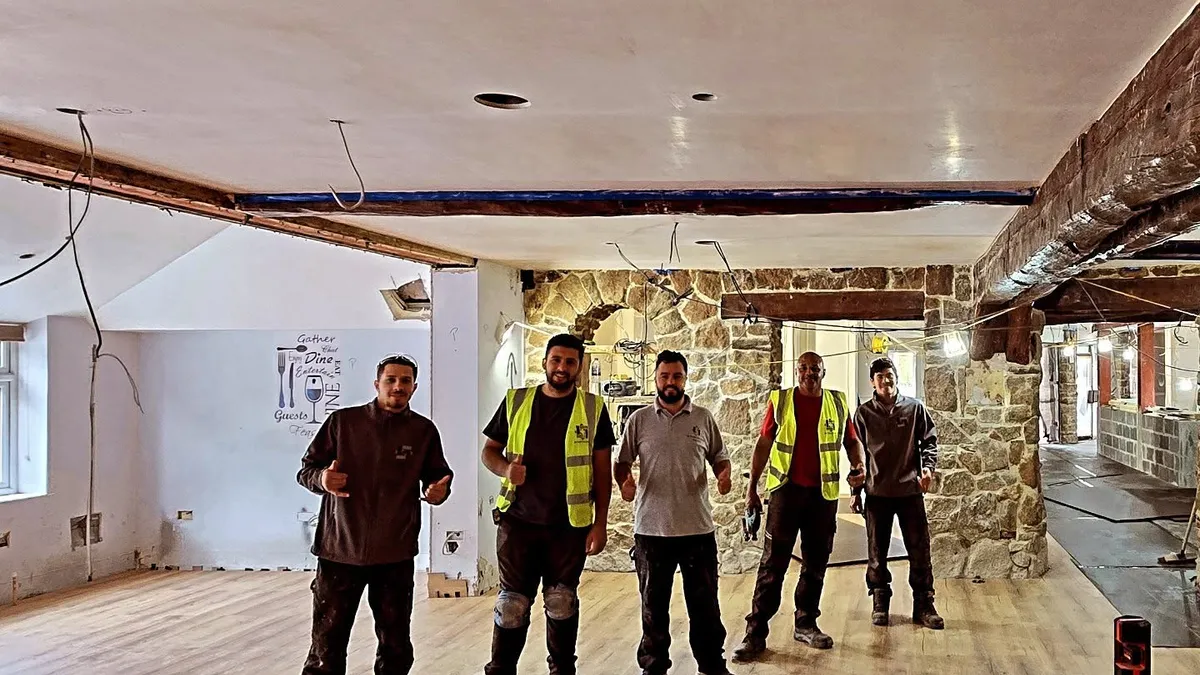Five people standing together in a renovation interior with wood-effect flooring and exposed stone walls.
