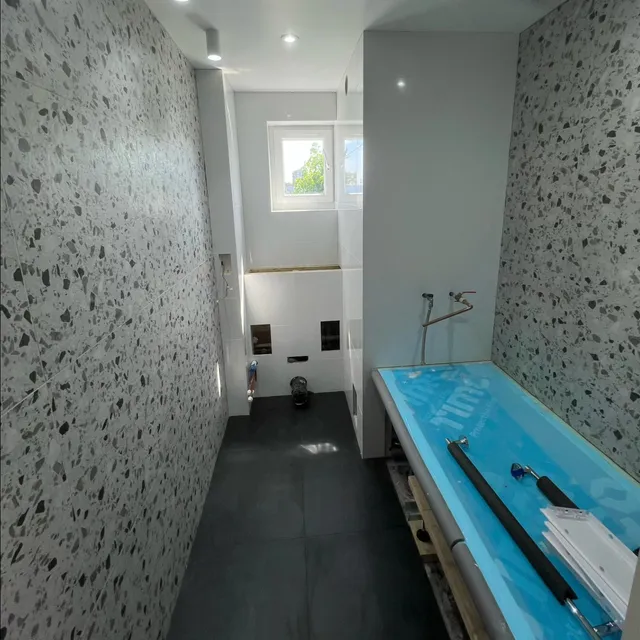 Narrow bathroom with a terrazzo-effect feature wall and dark floor tiles.