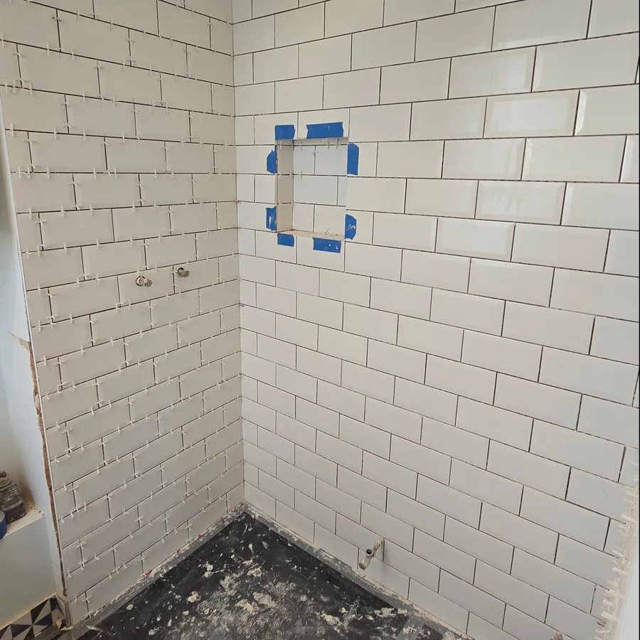 White rectangular wall tiles installed around a recessed shower niche with spacers.