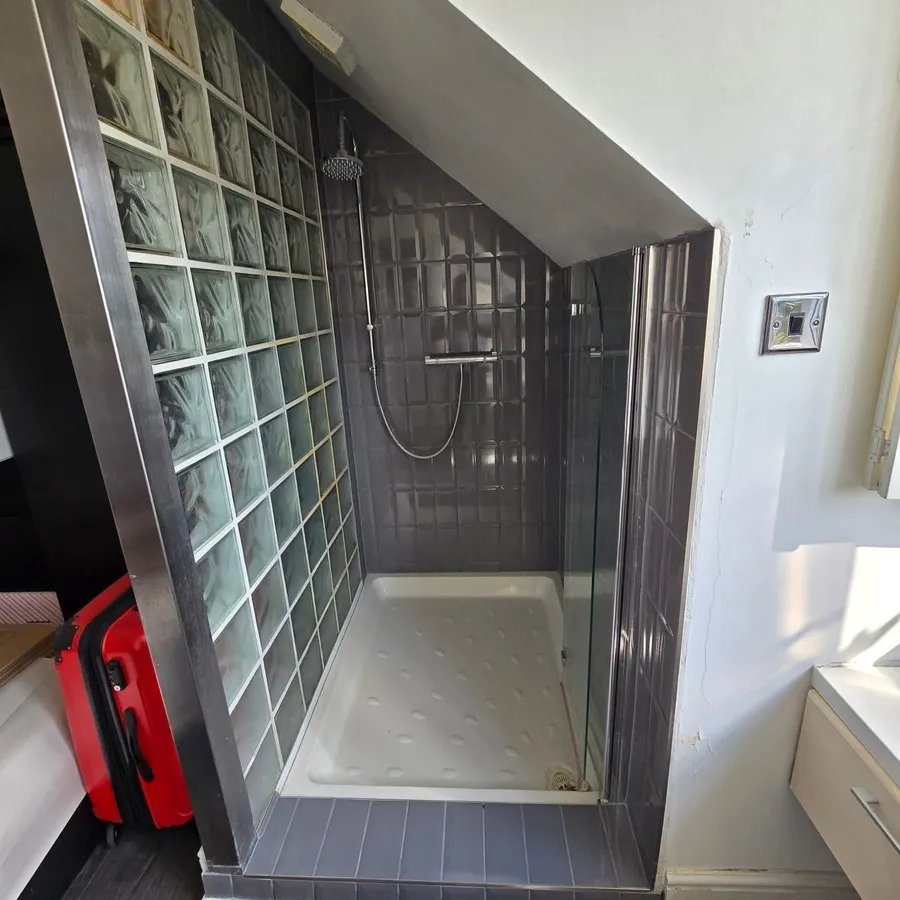 Walk-in shower under a sloped ceiling with vertical grey tiles and a glass-block side wall.